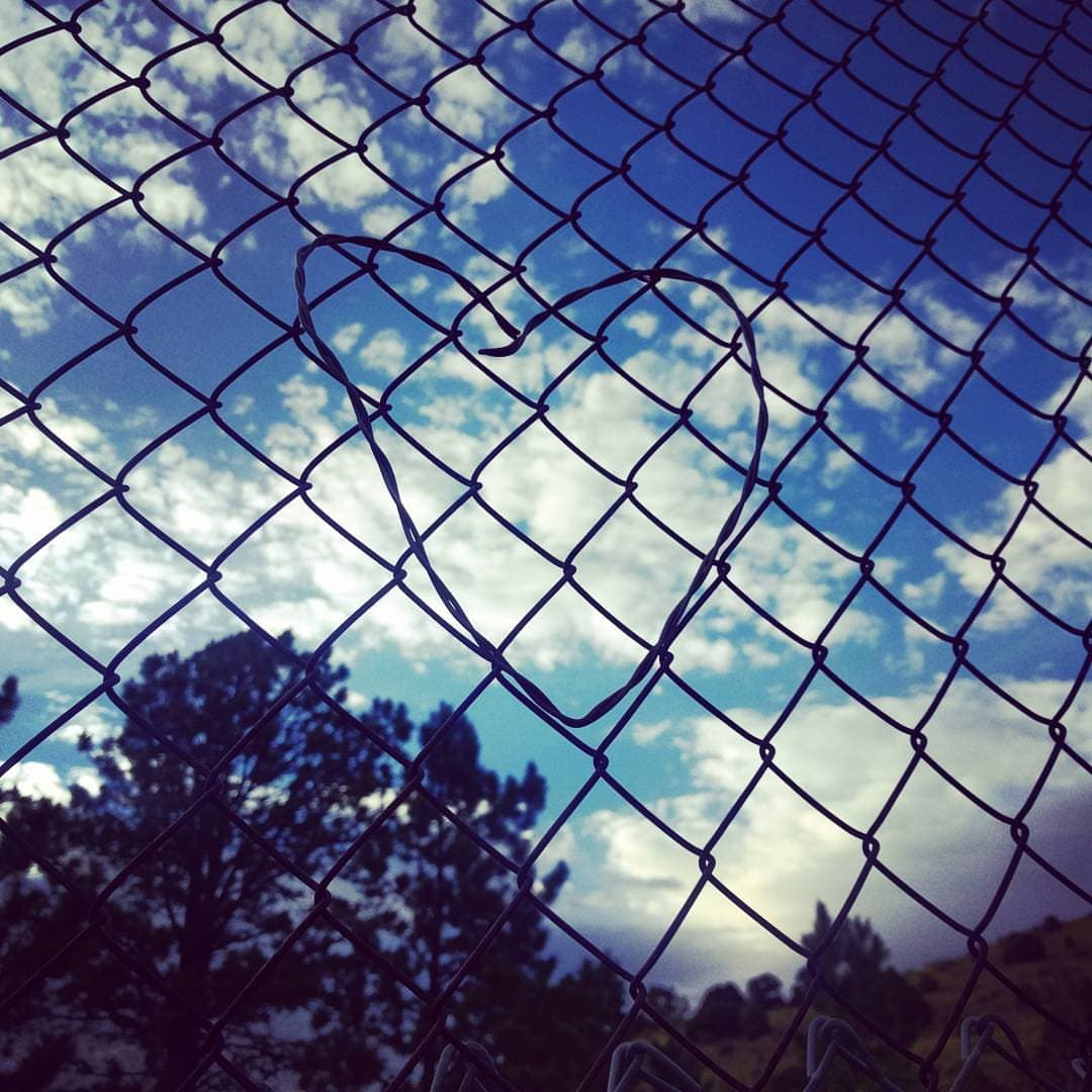 A heart made from bent wire and woven into a chain link fence